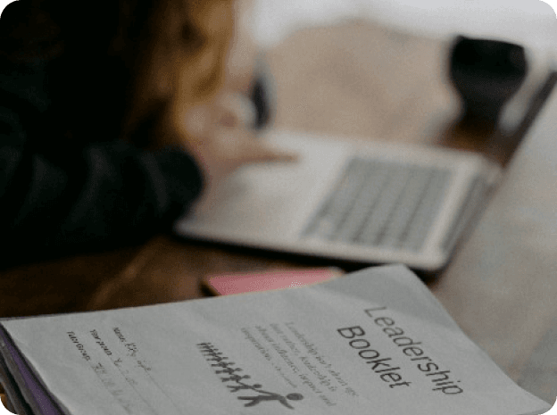 Apostila de estudo em primeiro plano e uma pessoa usando o notebook ao fundo