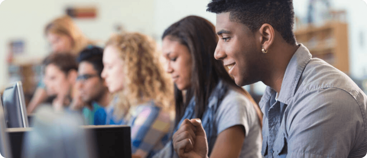 Estudantes sorrindo enquanto estudam em computadores numa sala de aula